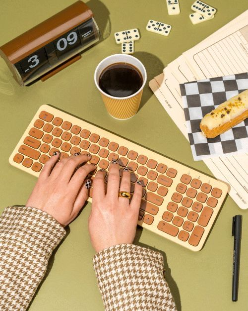 Hands typing on a retro keyboard beside a notebook and coffee